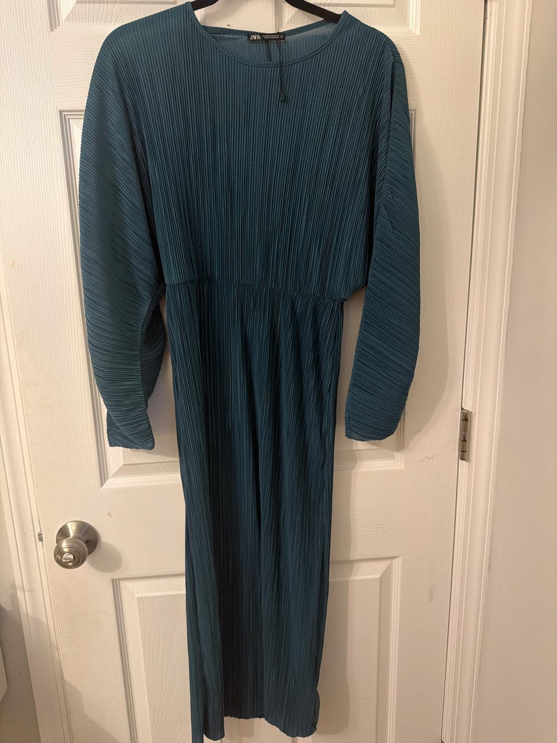 Long-sleeved pleated blue dress hanging on a white door.