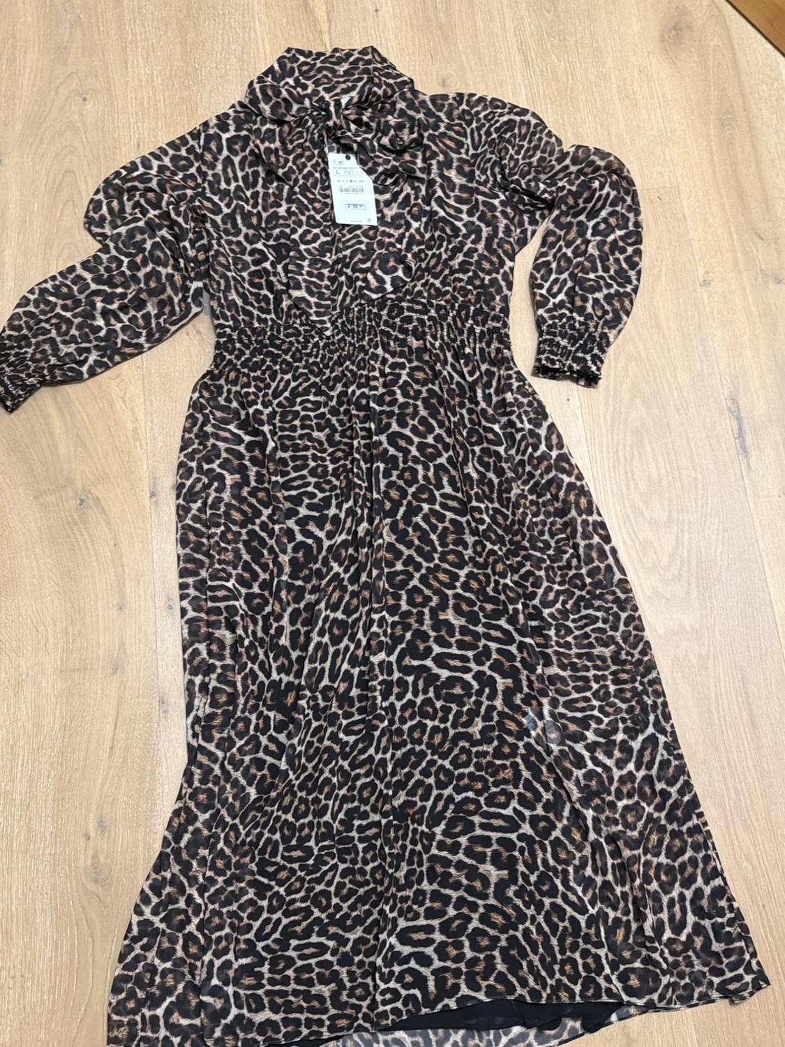 Long animal print dress on a light wood background. Visible label on the collar with price and size details.