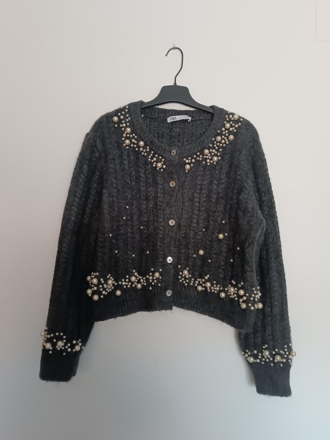 Dark grey cardigan with decorative pearls on the collar, cuffs, and bottom hem, hanging on a black hanger. Visible label: ZARA.