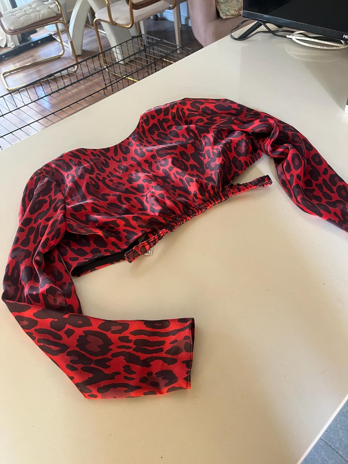 Red and black animal-print satin crop top with long sleeves and a gathered hem, on a table in a domestic setting.