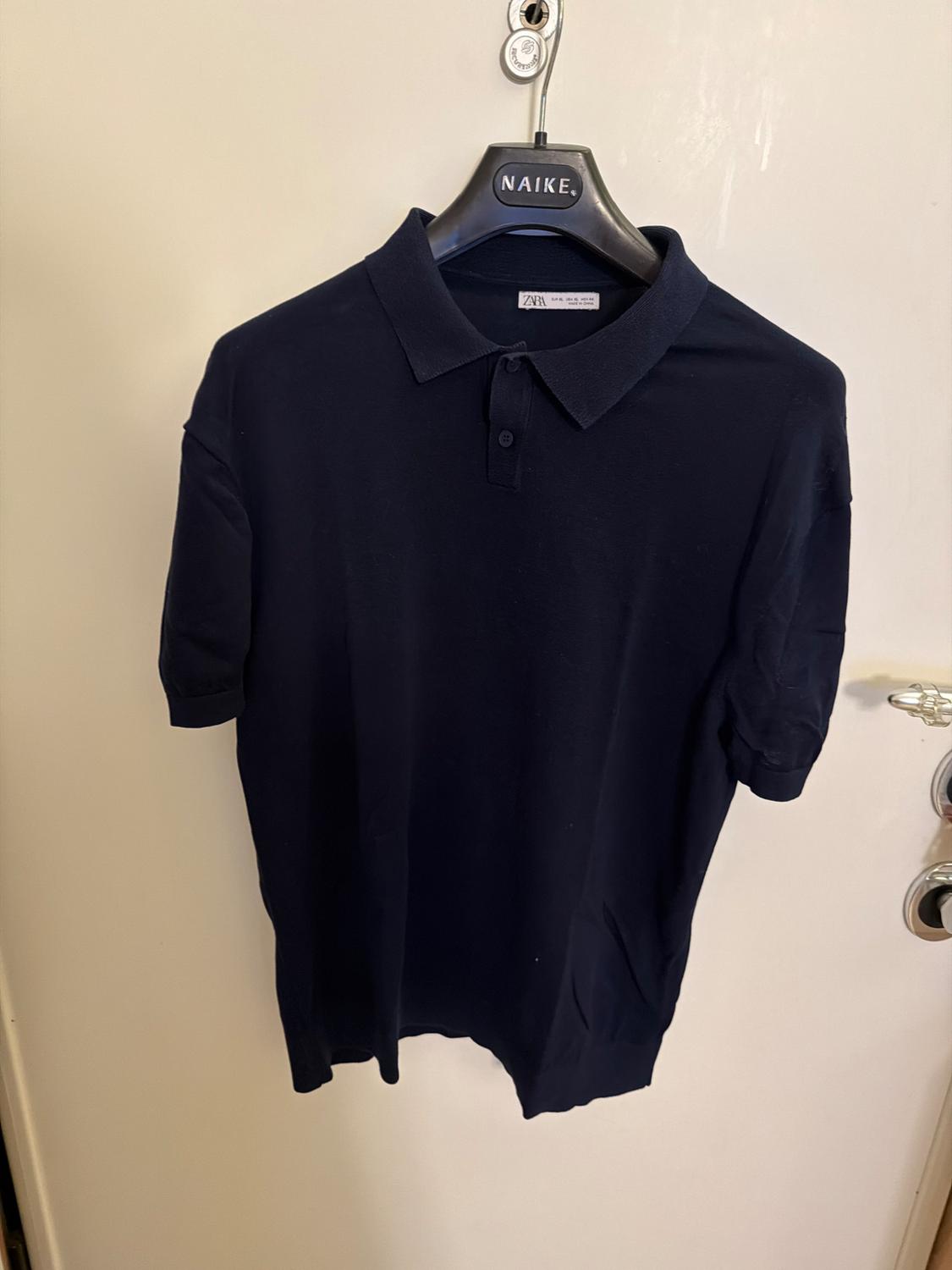 Dark blue polo shirt hanging on a black hanger with the word "NAIKE". White background and visible label on the collar.