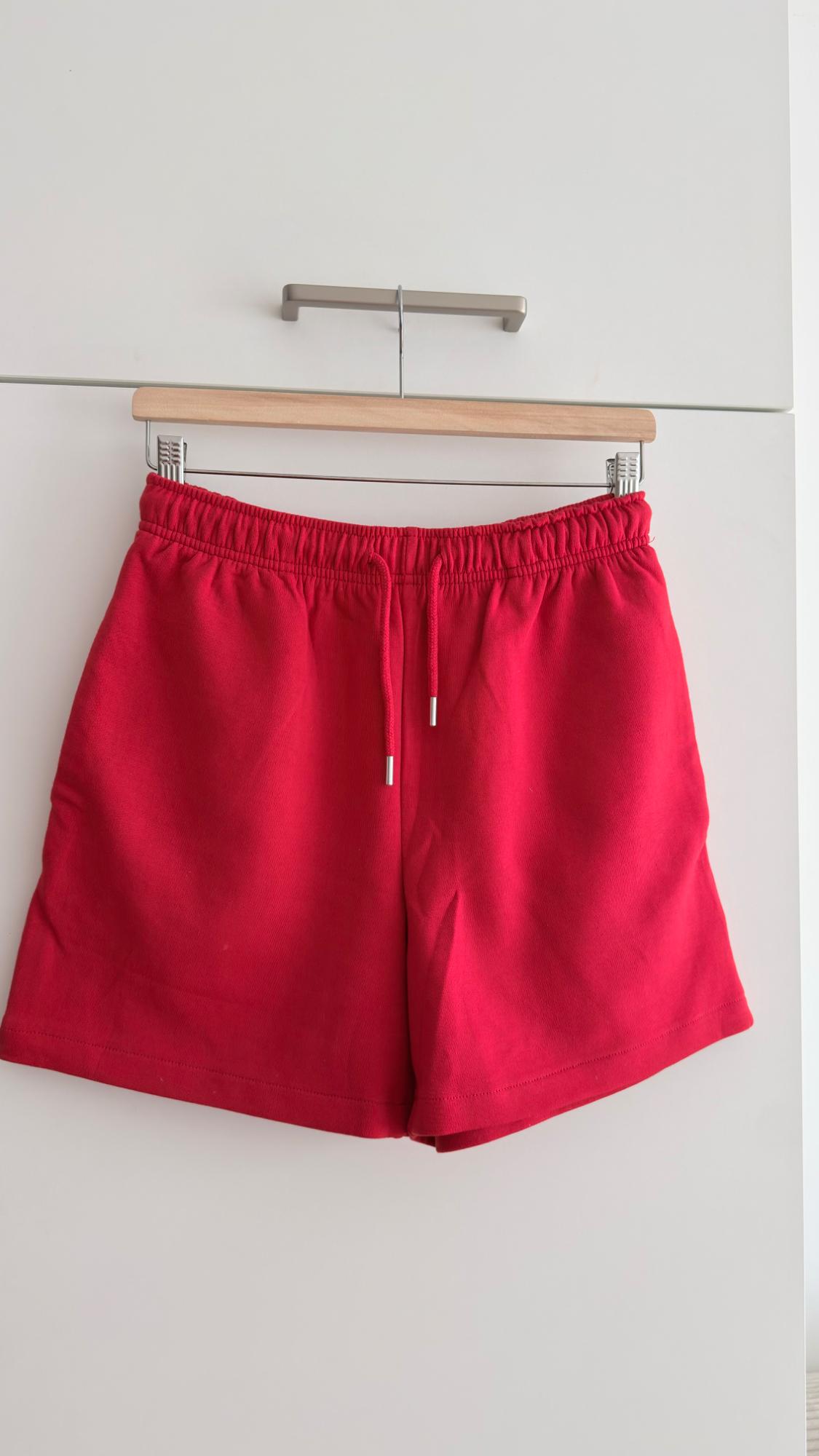 Red shorts hanging on a wooden hanger against a white background.