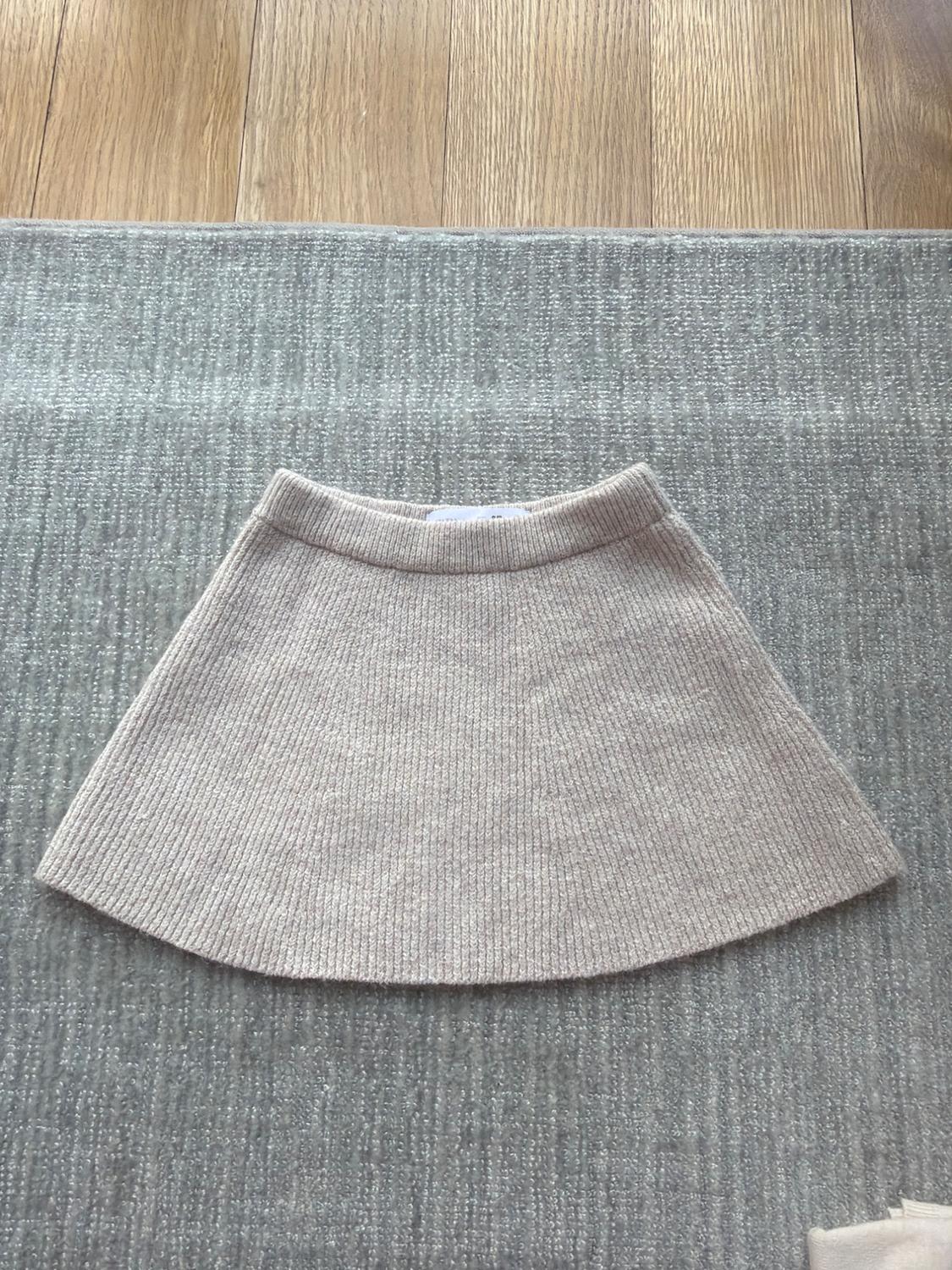 Short beige knitted skirt on a grey rug, with a light wooden floor background.