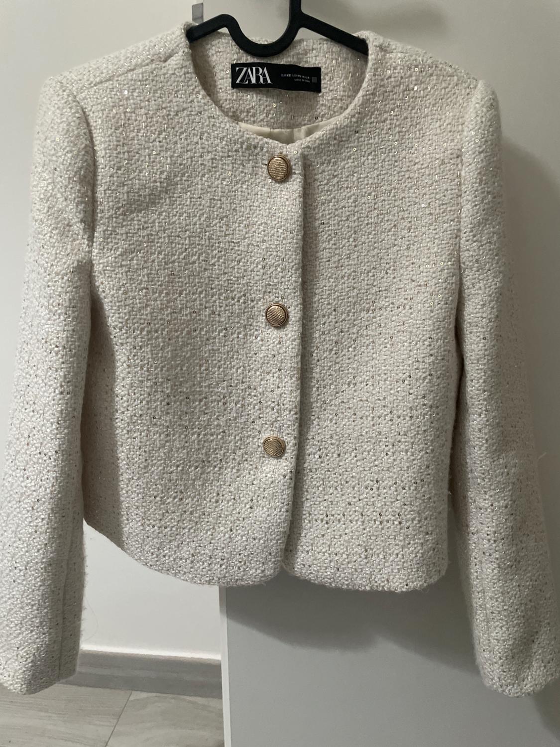 Cream-coloured textured fabric jacket with three gold buttons, hanging on a black hanger. Visible label: ZARA.
