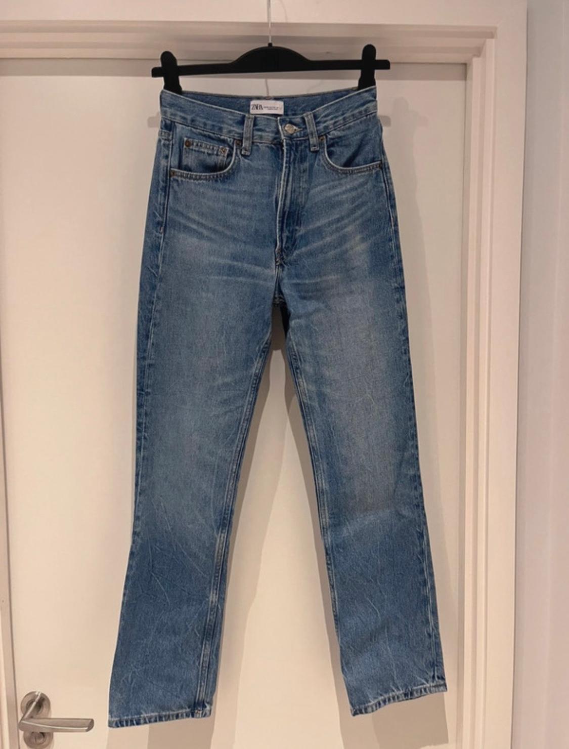 Blue jeans hanging on a black hanger over a white door. Label visible on the waistband.