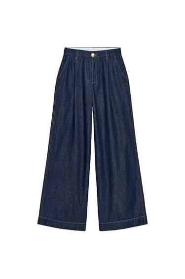 Front view of dark indigo, wide-leg trousers with a high waist, side pockets, pleats, and front closure with a metal button.