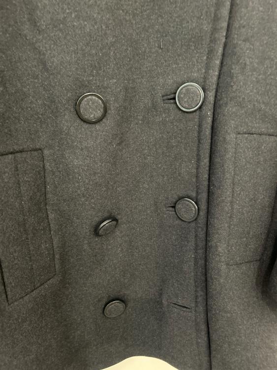 Dark grey double-breasted coat with side pockets. Soft-textured fabric and large buttons in the foreground.