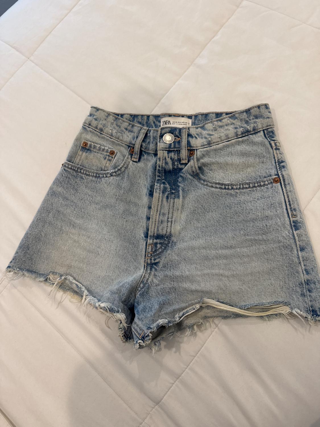 Light blue denim shorts with a frayed hem over a white quilt. Tag visible at the waist.