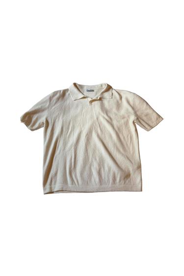 Soft cream-colored knit polo shirt with short sleeves and a classic collar,
laid flat on a white background.