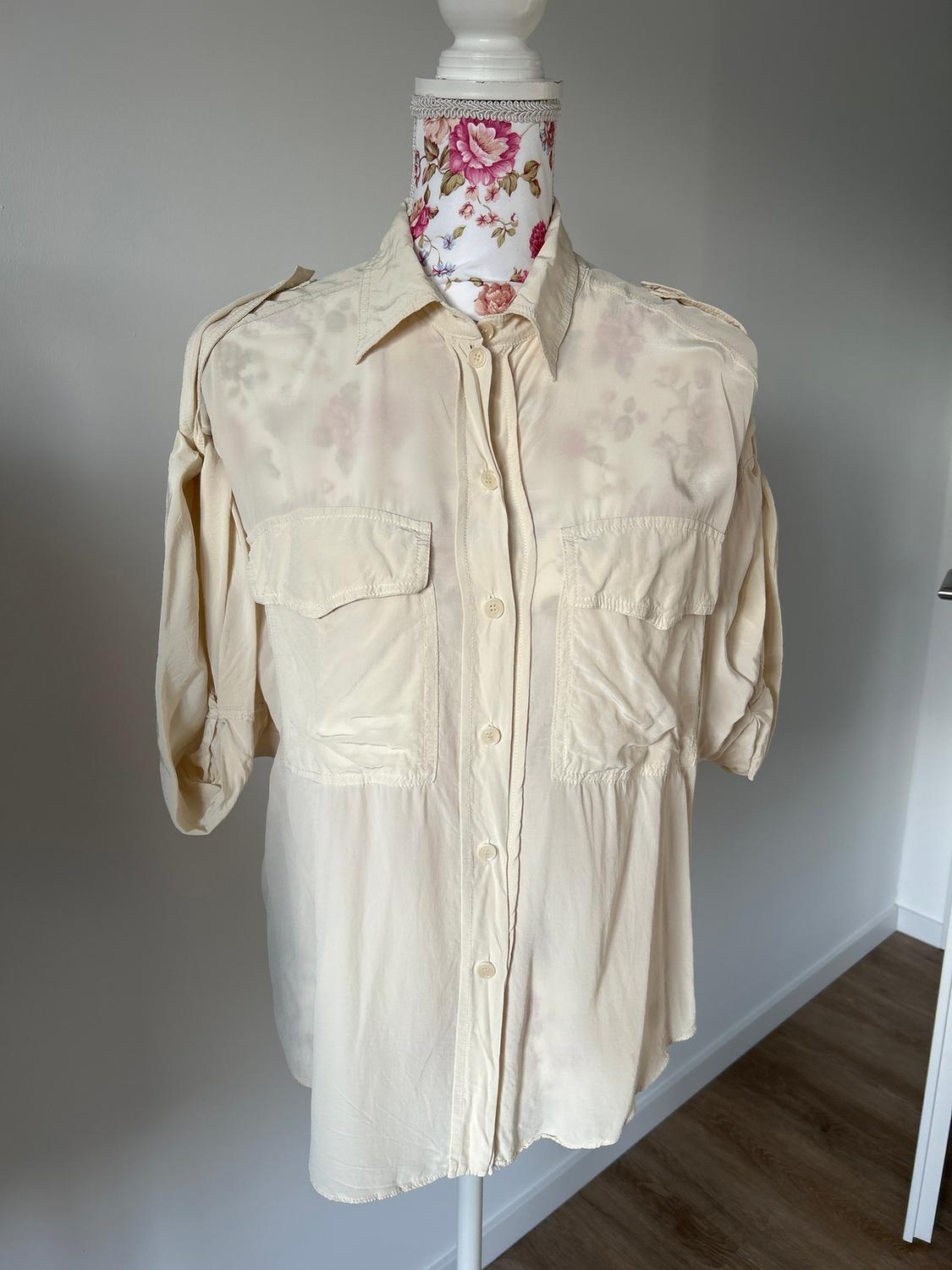 Mannequin with a long-sleeved beige shirt and front pockets, on a neutral background. The mannequin's neck has a floral print.