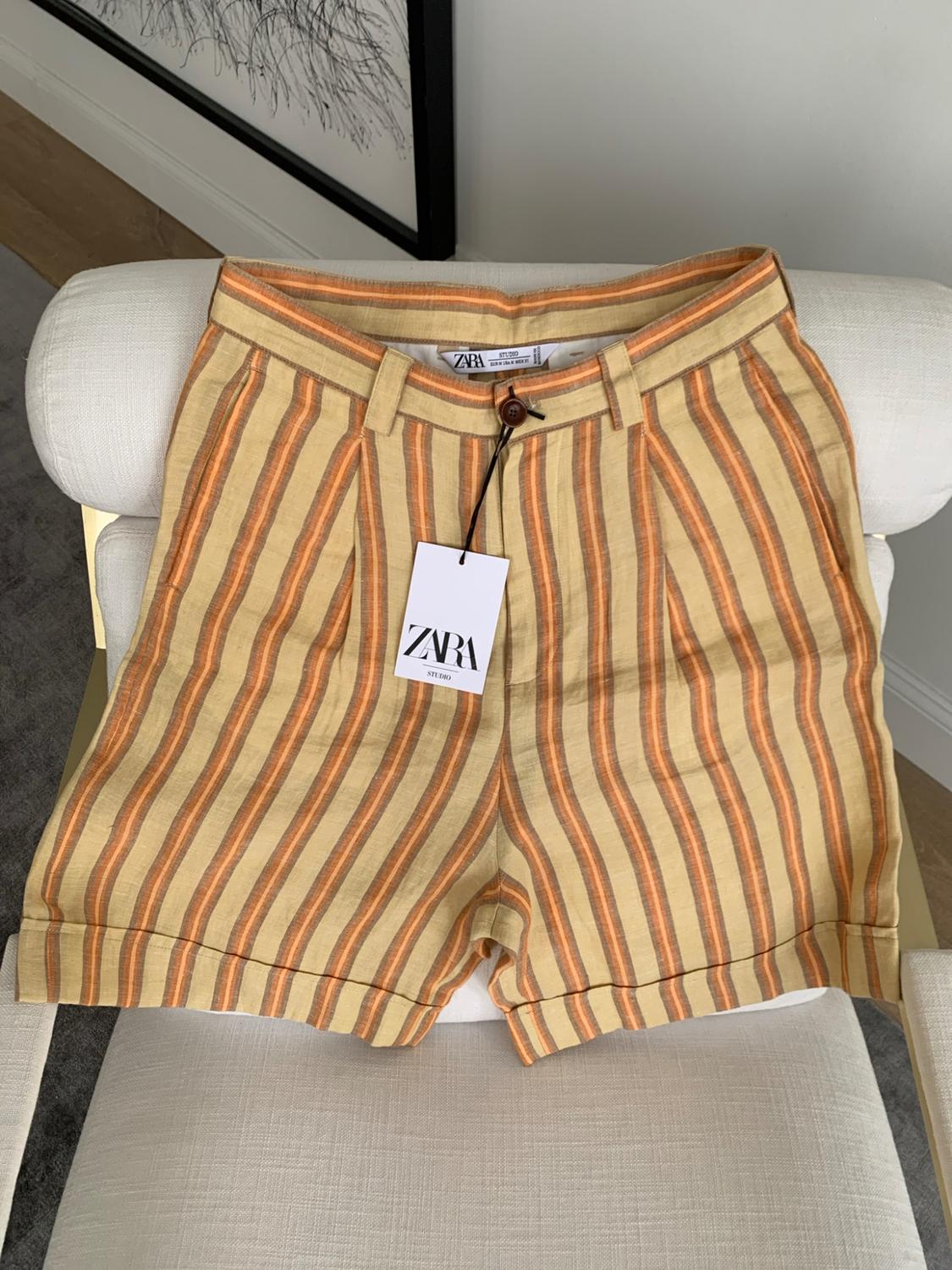 Shorts with yellow and orange vertical stripes on a white chair. Label with the text ZARA STUDIO.