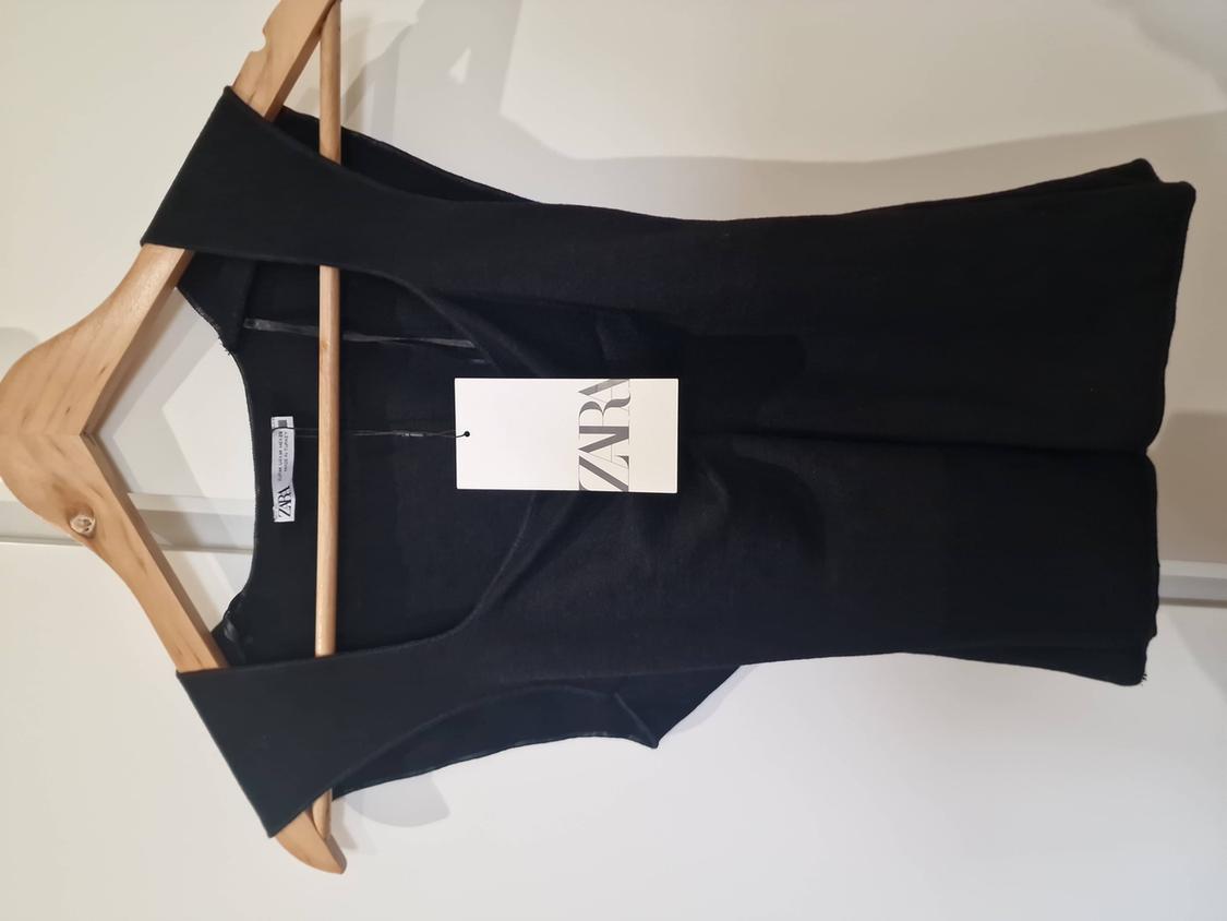 Black sleeveless top hanging on a wooden hanger, with a white label that reads "ZARA". White background.