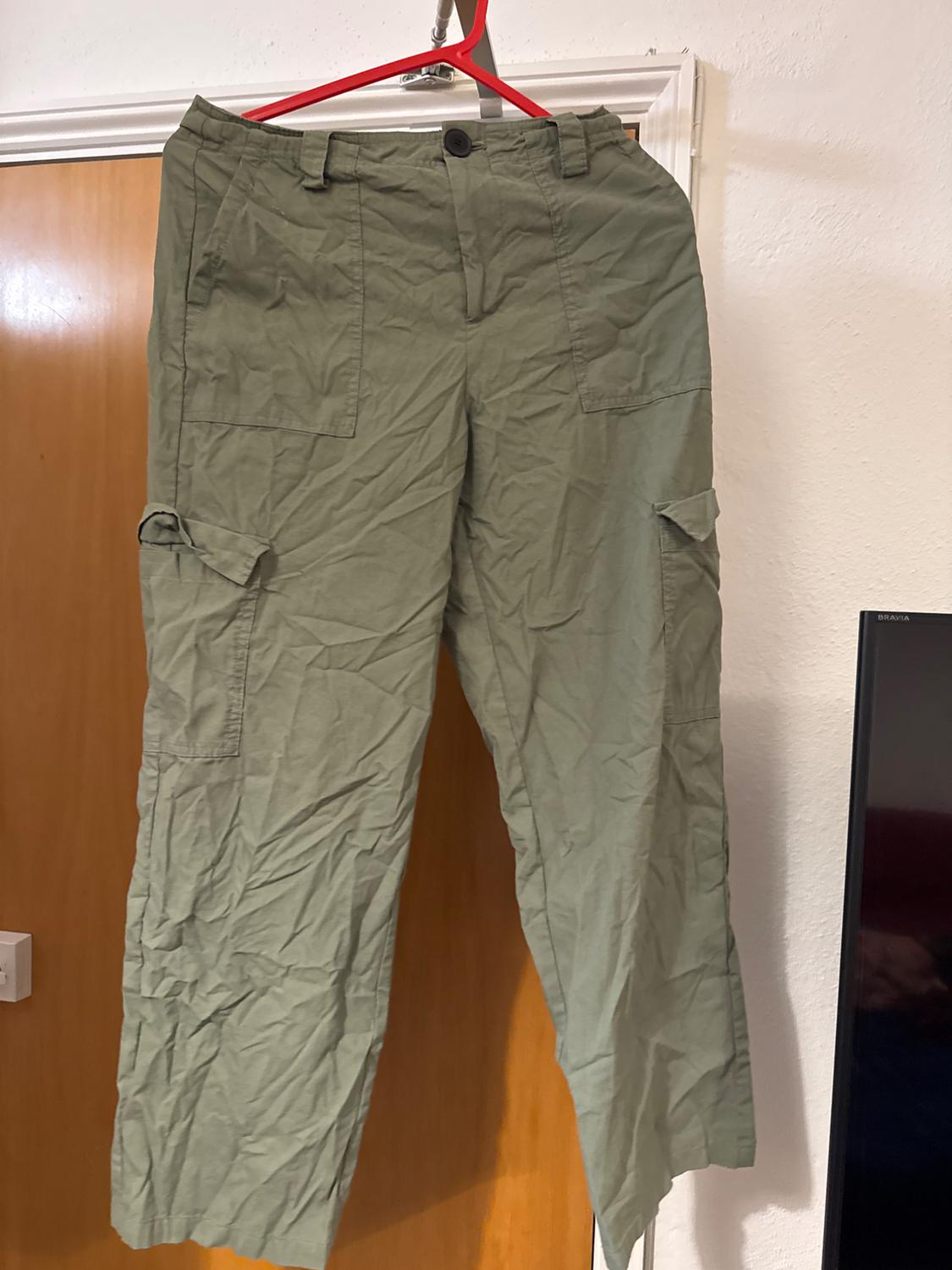 Crinkled olive green cargo trousers hanging on a red hanger in front of a light wood door.
