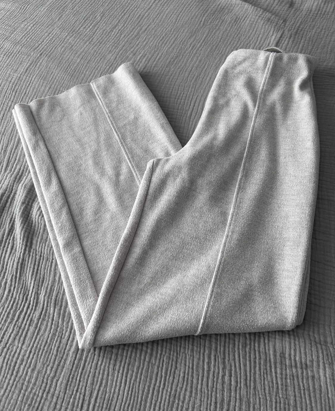 Grey trousers folded on a grey textured surface, showing stitching details and soft fabric.