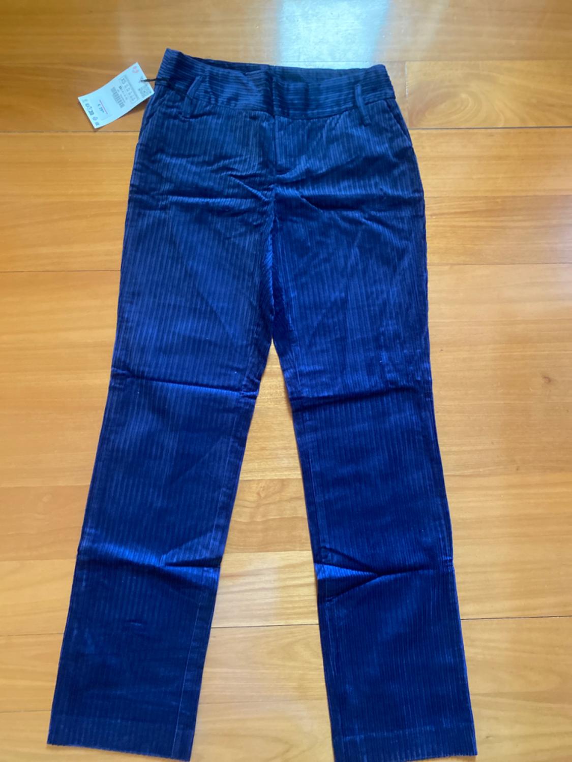 Dark blue corduroy trousers with a visible label, placed on a light wooden floor.