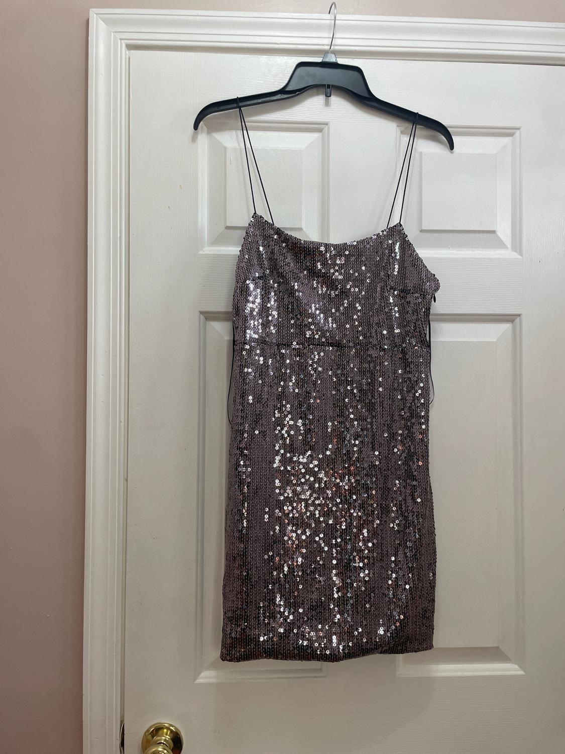 Short sequin dress with thin straps, hanging on a black hanger over a white door with a gold knob.