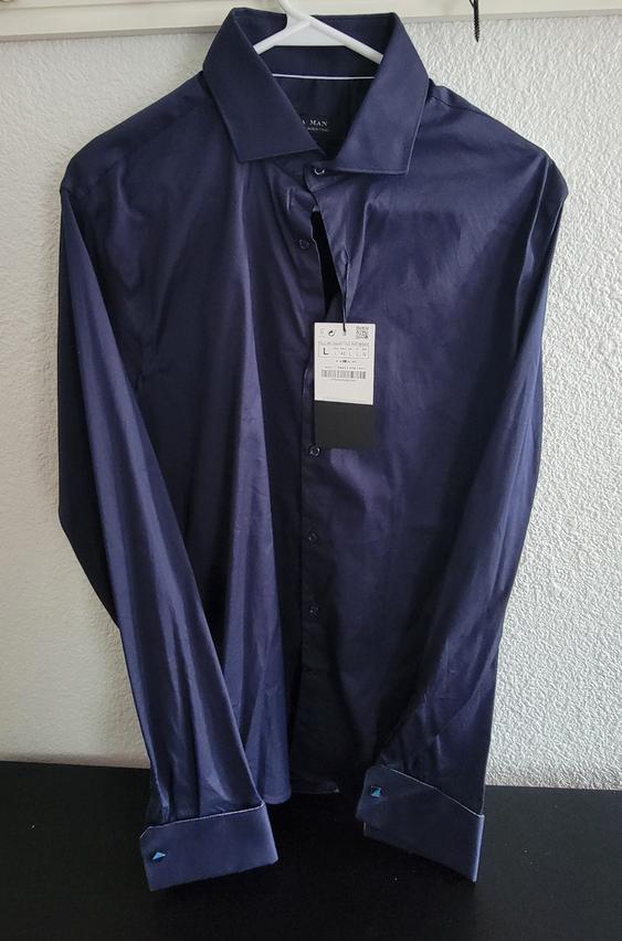 Dark blue shirt hanging on a white hanger, with a visible label in the center. White wall background and black surface.