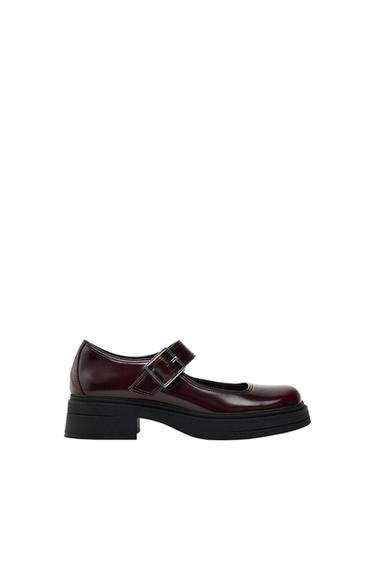 Burgundy shoe with a strap and silver buckle fastening, thick black sole, on a white background.