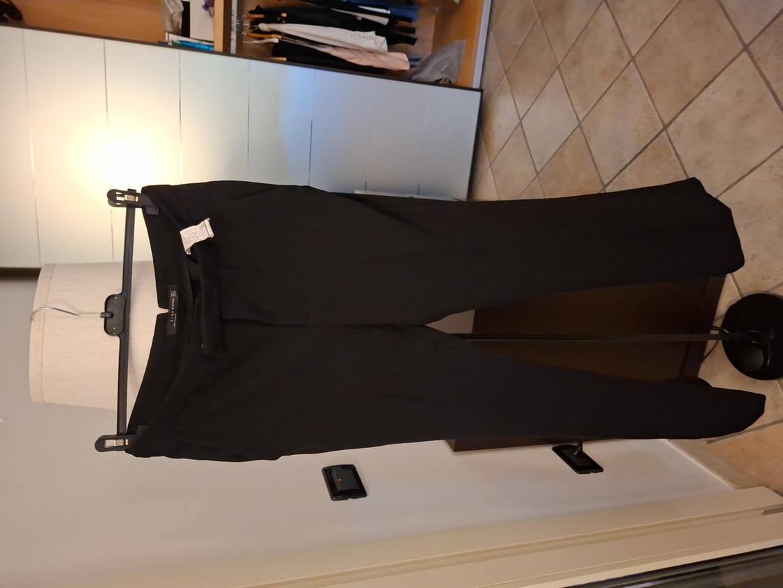 Black trousers hanging on a clothes rail in a room with a tiled floor and a wardrobe with clothes in the background.