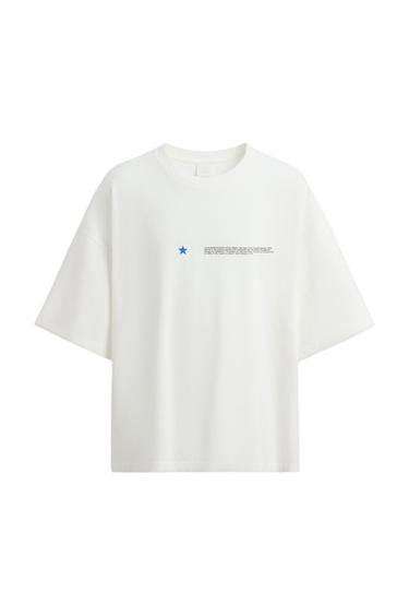 Λευκό T-shirt με ένα μπλε αστέρι και μικρό κείμενο στο στήθος. Μίνιμαλ σχέδιο σε λευκό φόντο.