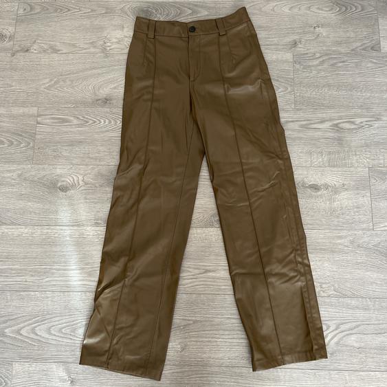 Straight-cut brown trousers with front pleats, a black button, and belt loops, on a light wooden floor.