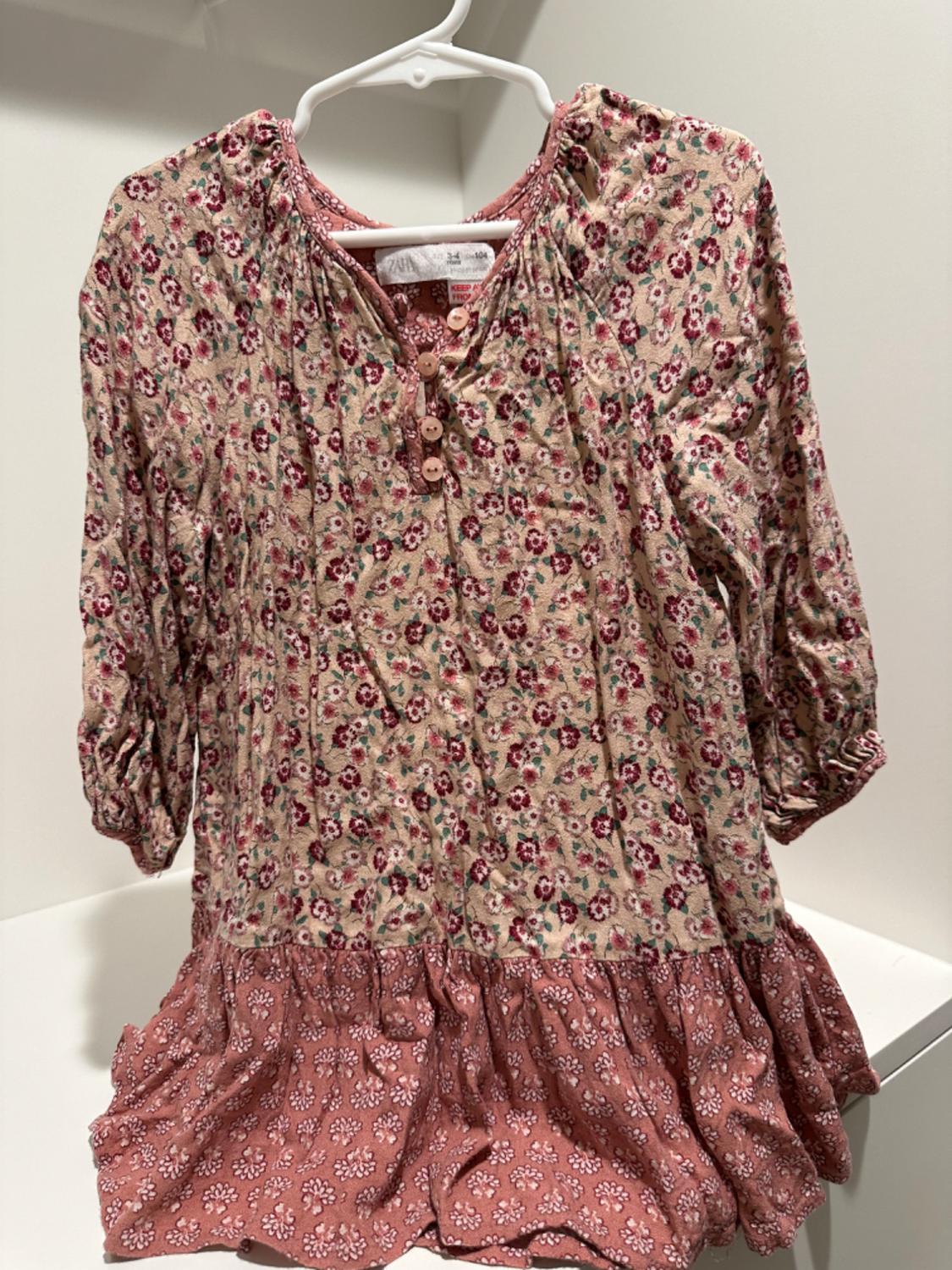 Front view of floral dress with buttons and ruffle hem, red and beige floral print.