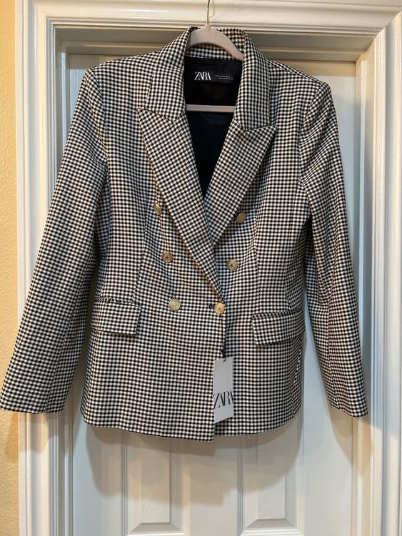 Black and white checkered jacket with gold buttons, hanging on a door. Visible tag with the text "ZARA".