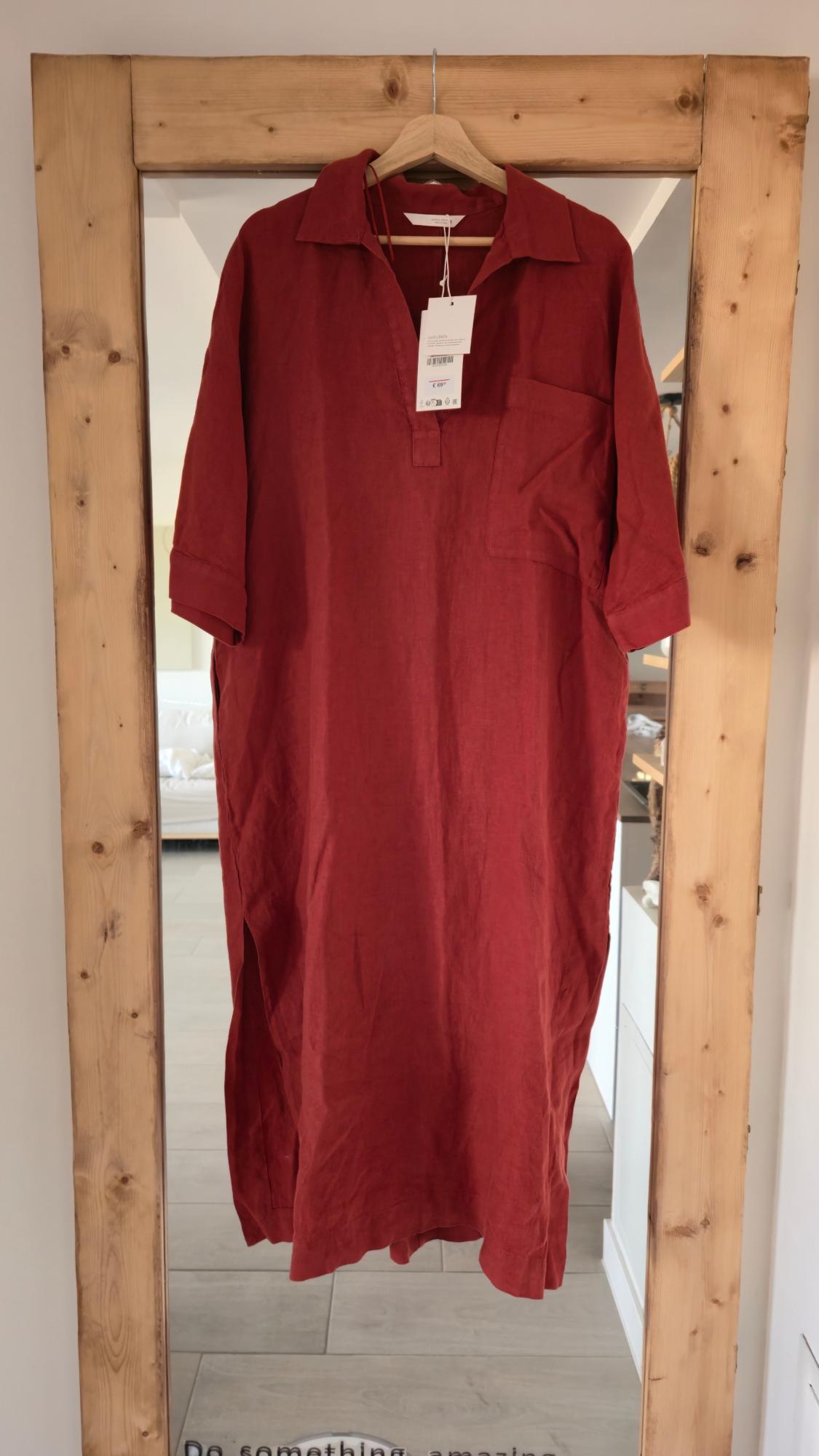 Red linen dress hanging on a wooden mirror. Visible label on the collar. Text on the floor: "Do something amazing".