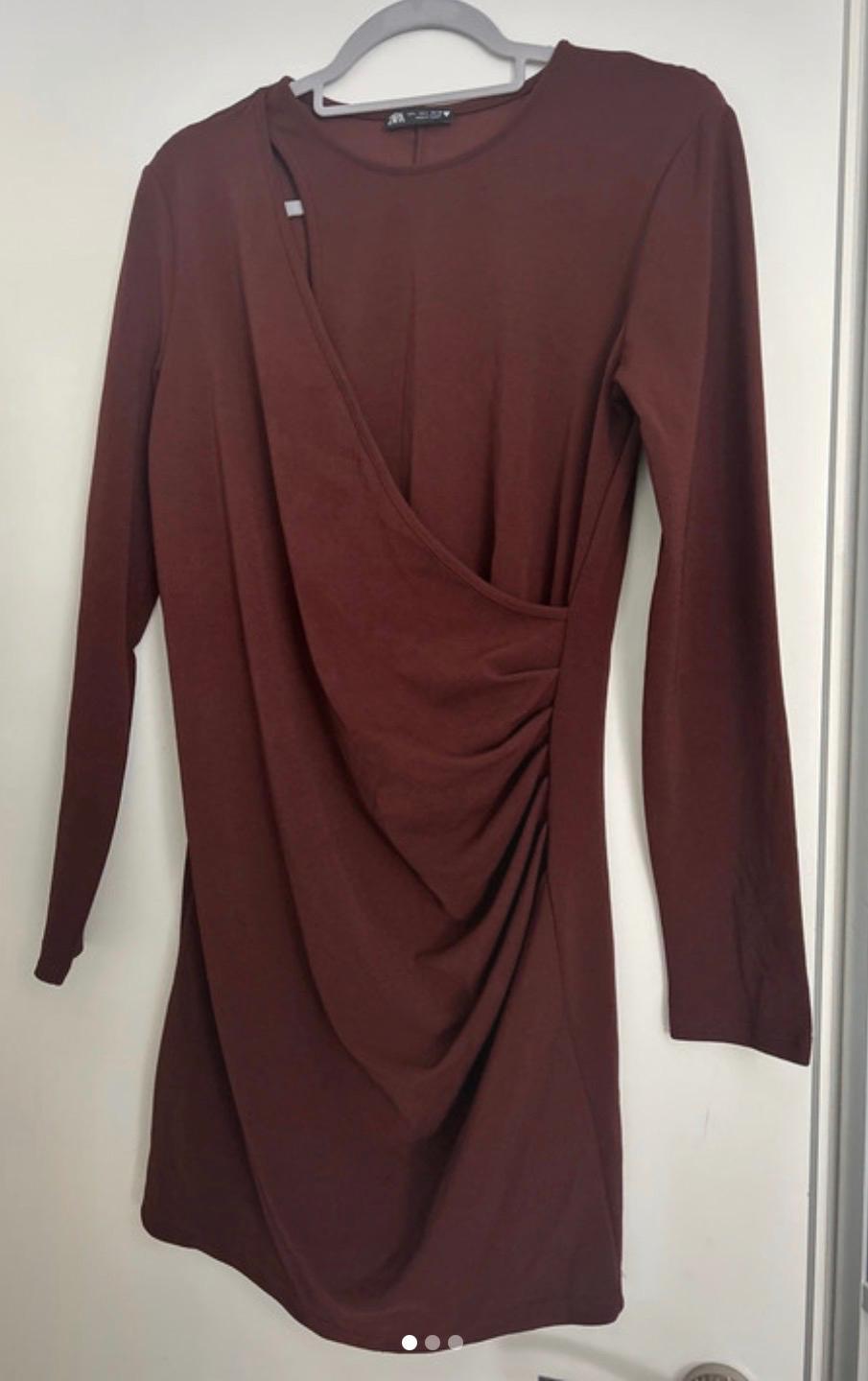 Brown long-sleeved dress with side ruching, hanging on a grey hanger over a white door.