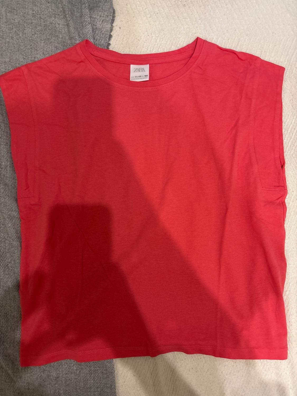 Red sleeveless t-shirt on a grey and beige textile surface. Visible label with the text "ZARA".