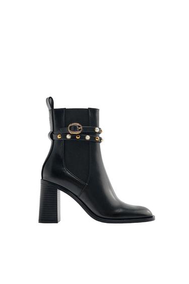 Side view of a black boot with a high heel and buckle and pearl embellishments.