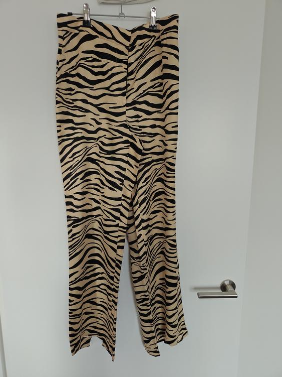 Animal print trousers in beige and black tones hanging on a hanger over a white door.