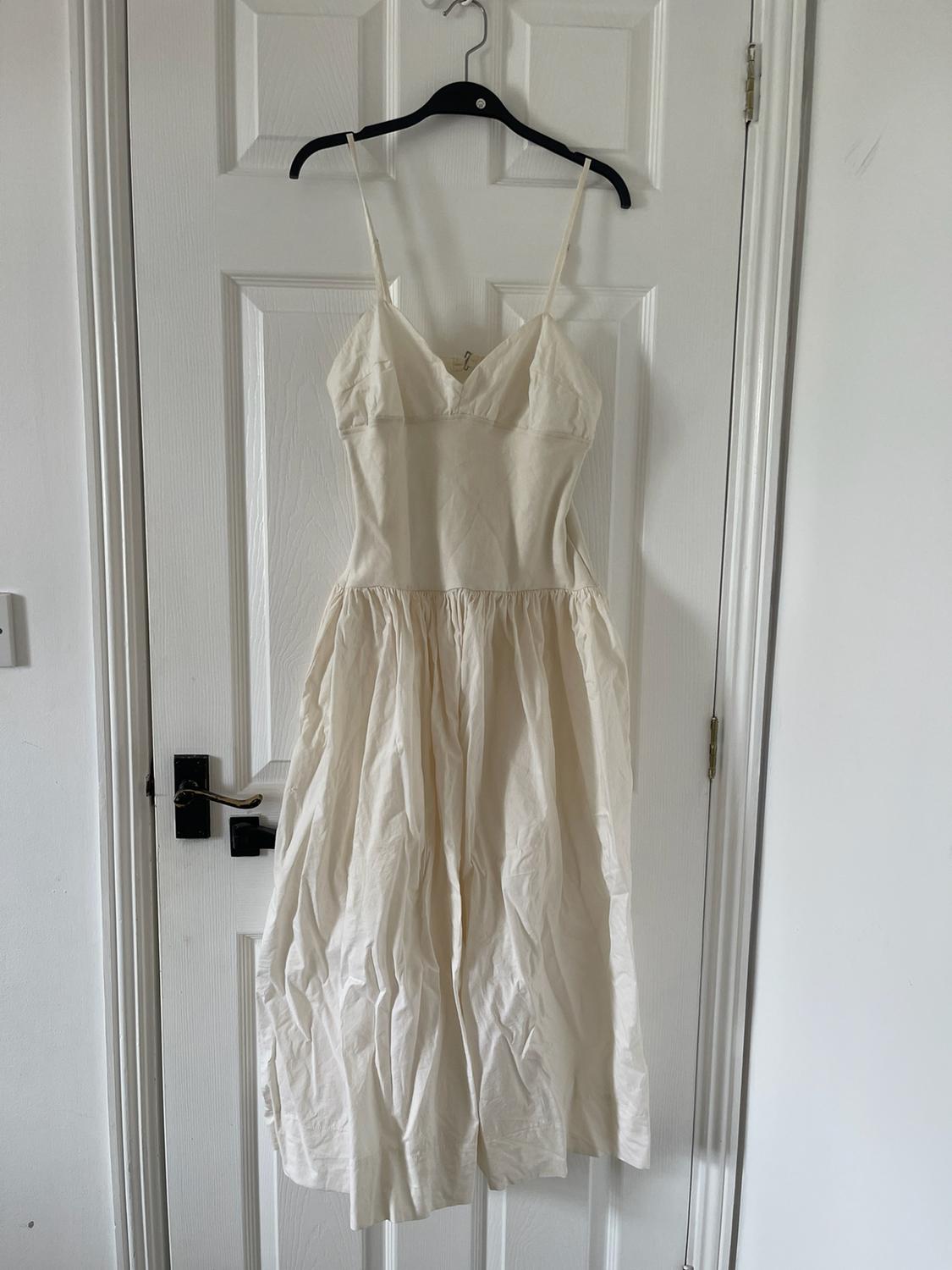 White dress with thin straps and a full gathered skirt, hanging on a black hanger on a white door.