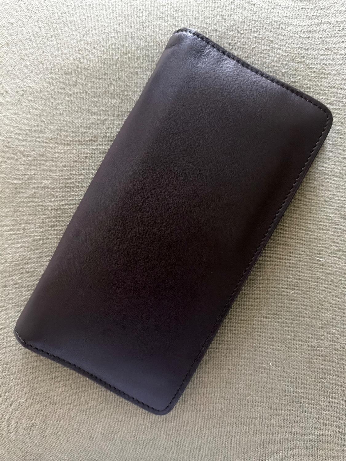 Dark brown leather wallet with a minimalist, rectangular design, placed on a light, textured fabric surface.
