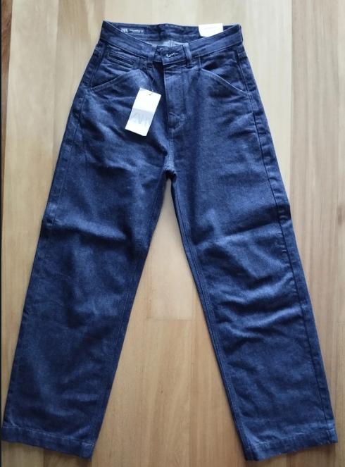 Blue wide-leg jeans with a white hanging tag, on a light wooden background.