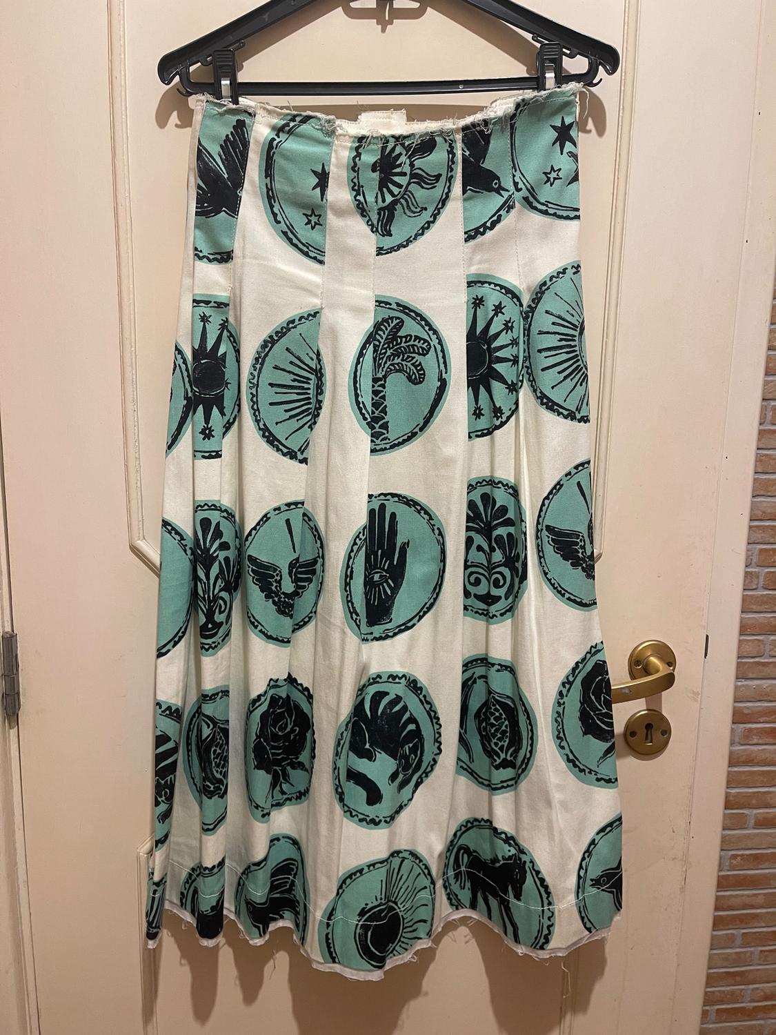 Hanging skirt with green and black circle print with symbols, over a light wooden door with a gold knob.