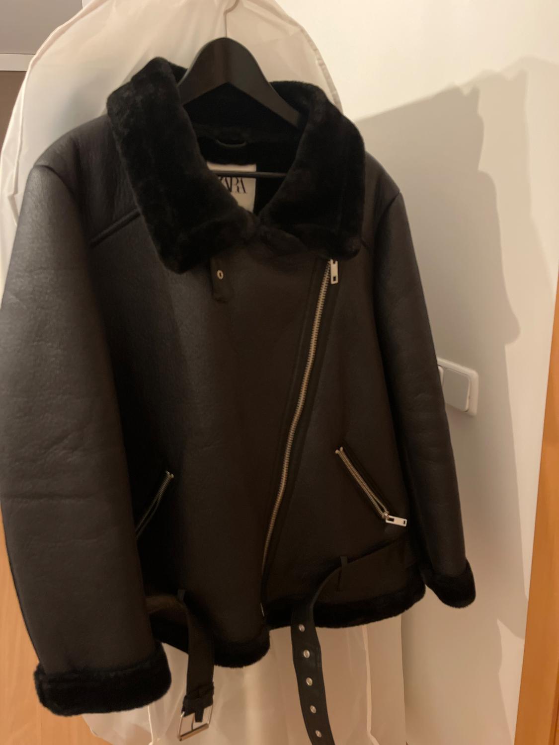 Black jacket with a diagonal zip and faux fur collar, hung on a black hanger over a white cover.
