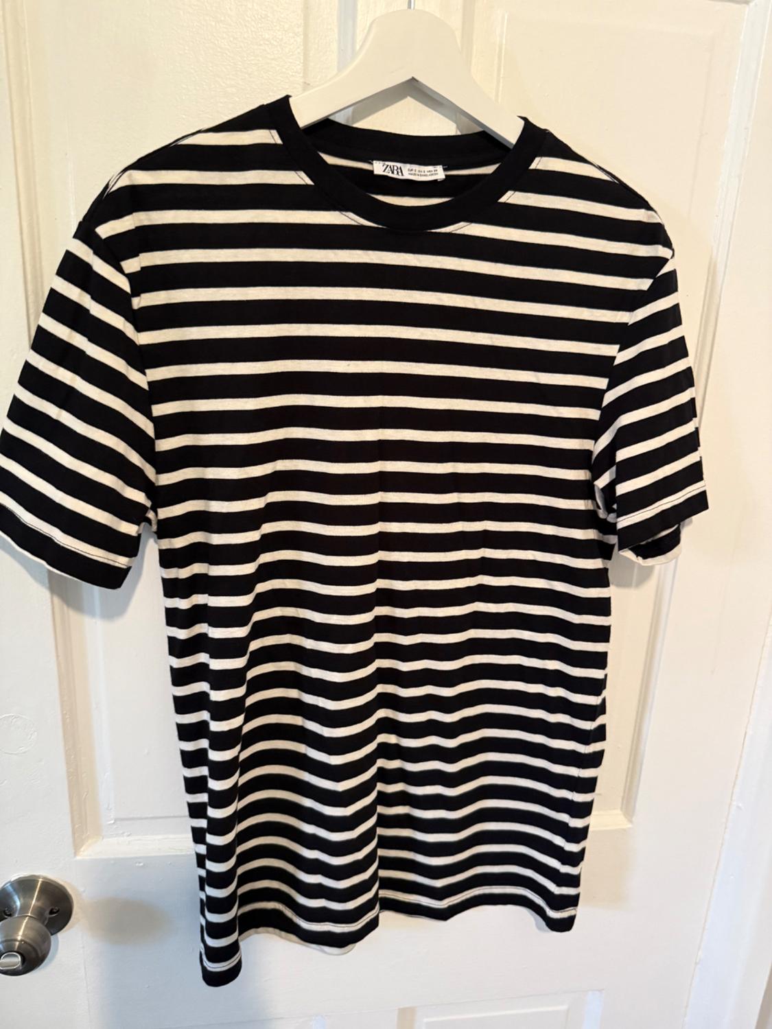 White and black horizontal striped T-shirt hanging on a white hanger over a white door. Label visible.