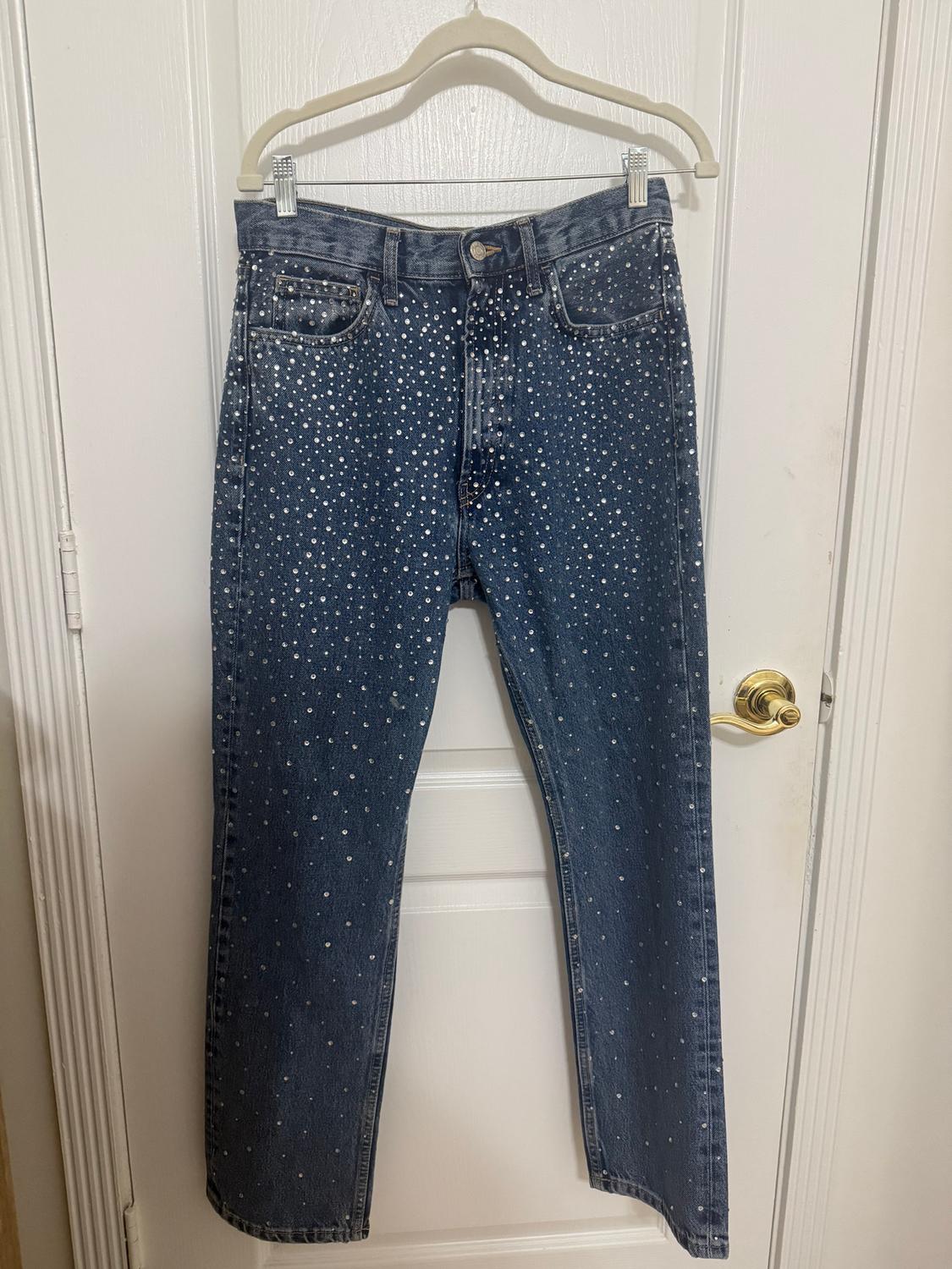 Blue jeans with shiny stud details hanging on a white hanger over a white door.