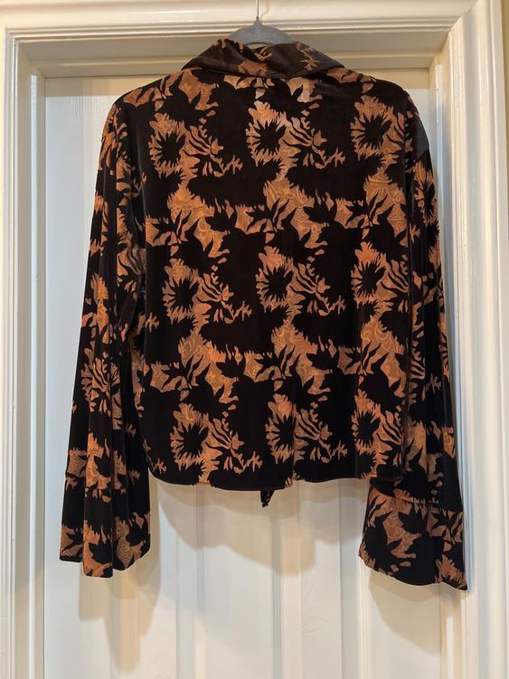 Black velvet jacket with brown floral print, hanging on a white door. Long sleeves and folded collar.