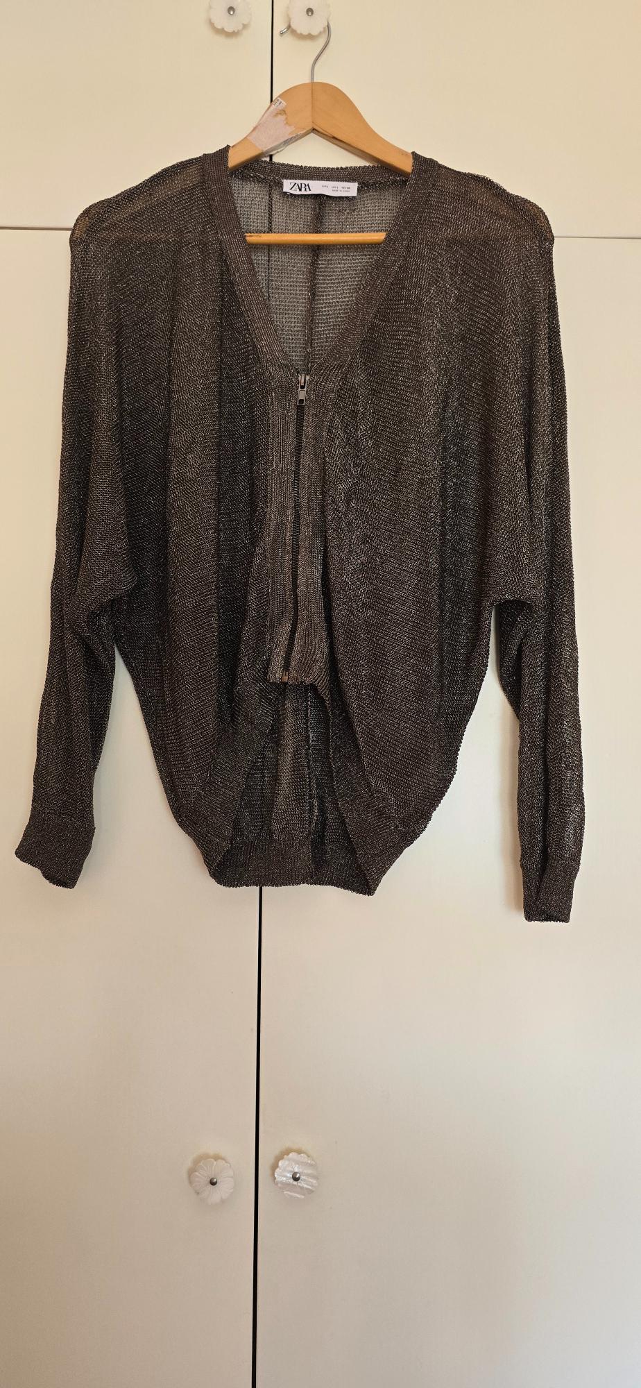 Dark sparkly knit jumper with a front zip, hanging on a wooden hanger against a white wardrobe. ZARA text visible.