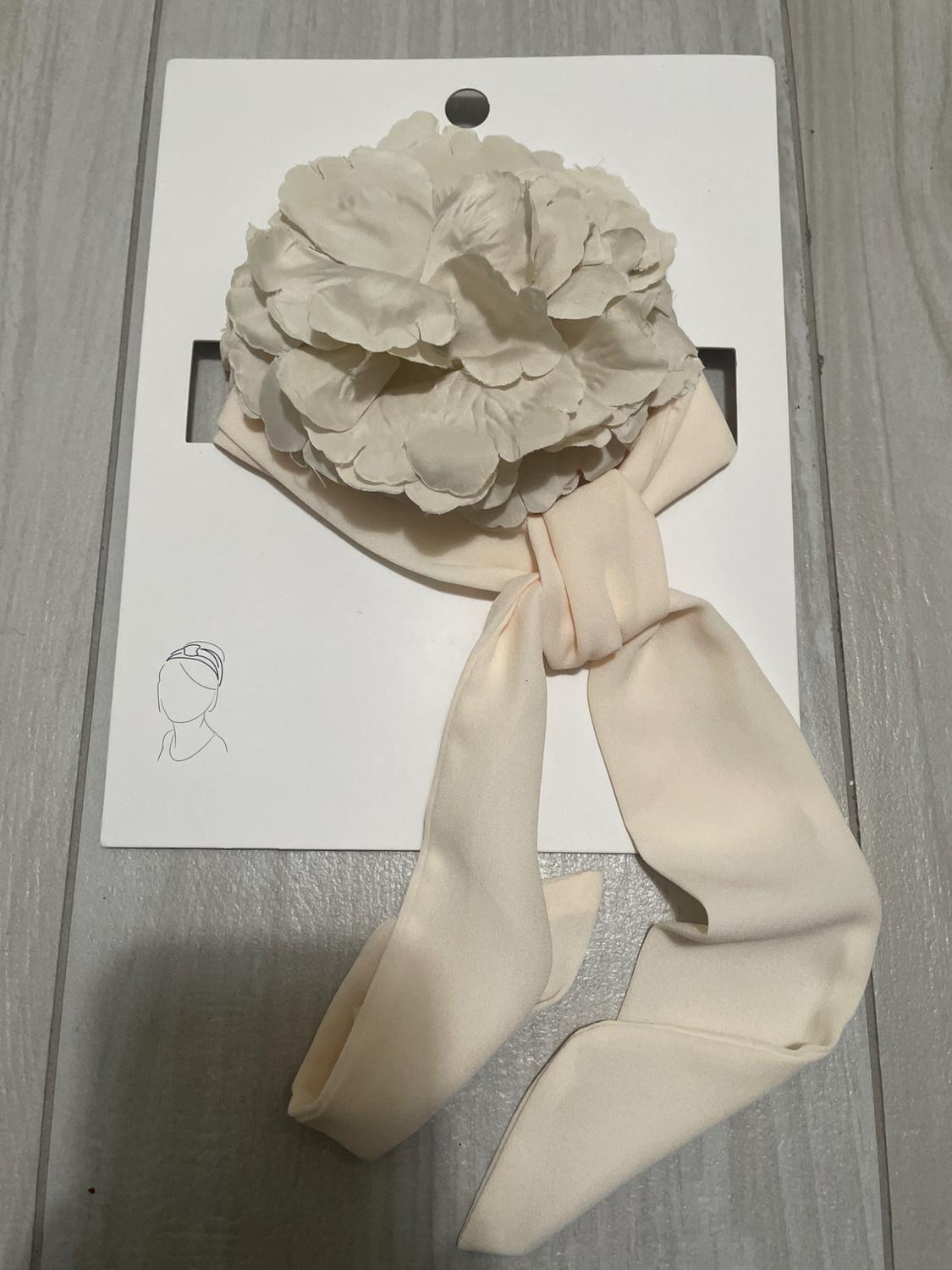Cream hairband with large flower on white card. Usage drawing in bottom left corner.