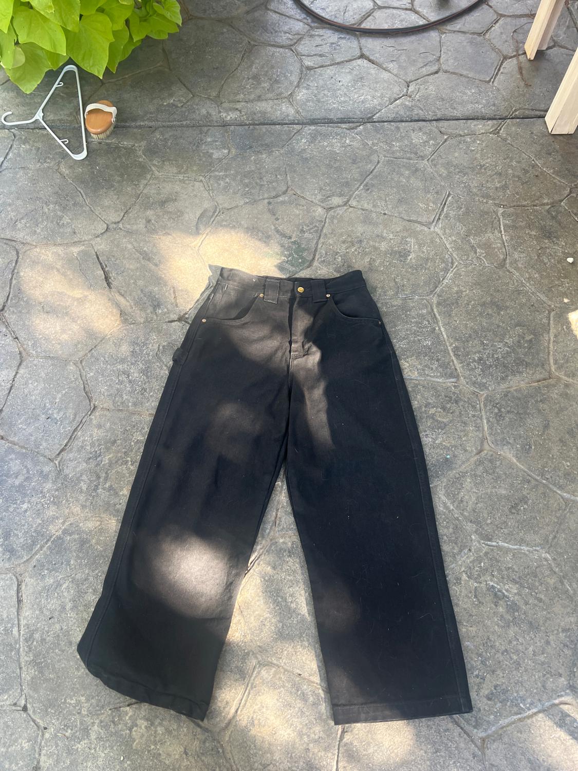 Black wide-leg trousers on an outdoor stone floor. Natural light with cast shadows, conveying a relaxed atmosphere.