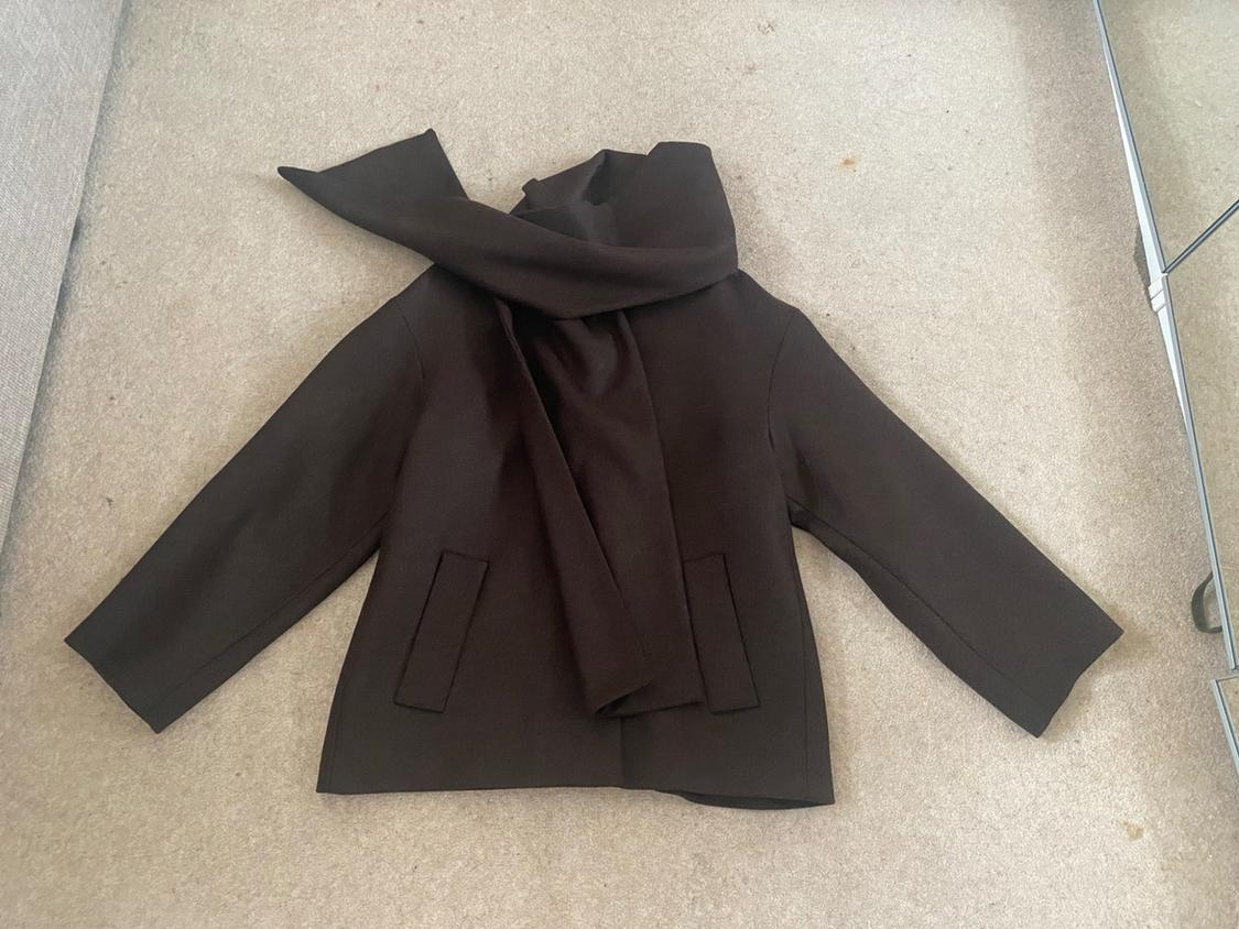 Dark brown jacket with a matching scarf, laid out on a beige rug in a relaxed home setting.