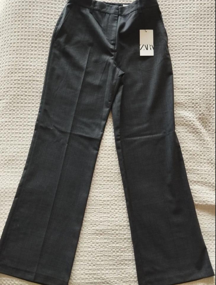 Dark grey tailored trousers with a front crease, laid flat on a light, textured surface. Label with the text ZARA.
