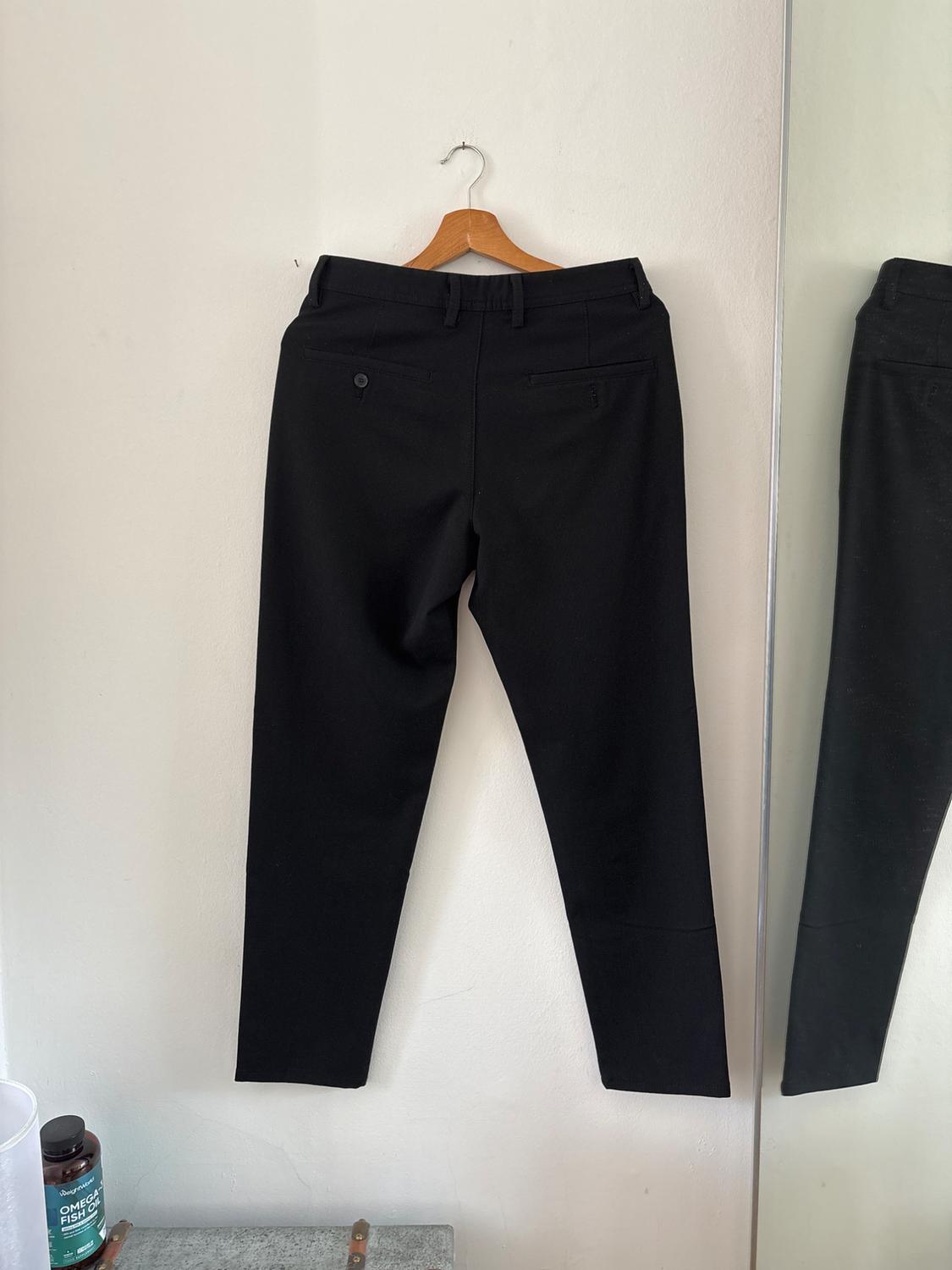 Black trousers seen from behind on a wooden hanger against a white wall. Next to a mirror and a jar with the text OMEGA FISH OIL.