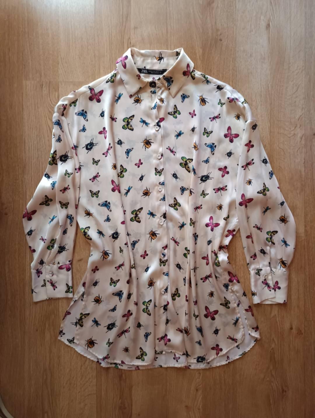 Cream-coloured long-sleeved shirt with an insect and butterfly print on a wooden floor. ZARA label.