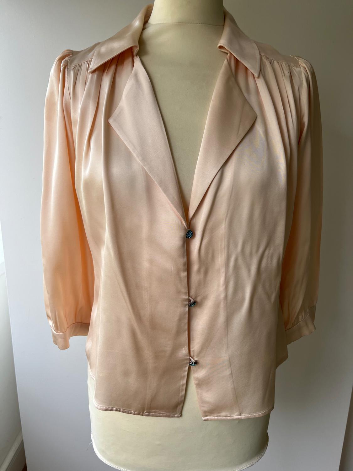 Peach-coloured satin blouse with a wide collar and three-quarter sleeves, buttoned at the front, displayed on a beige mannequin.