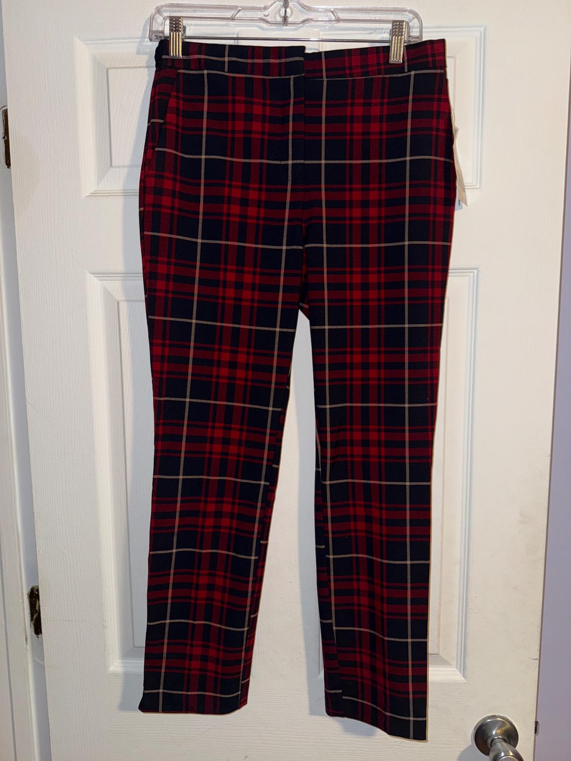 Red and black checked trousers hanging on a clear hanger over a white door.