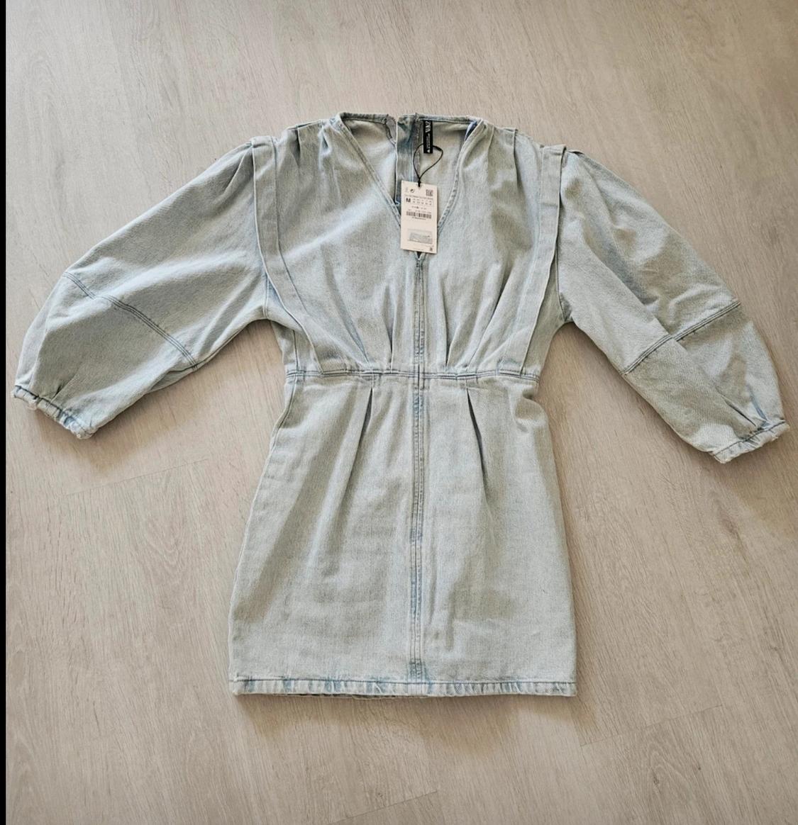 Light blue denim mini dress with a V-neck, puffed sleeves and a fitted waist, laid out on a light wood floor.